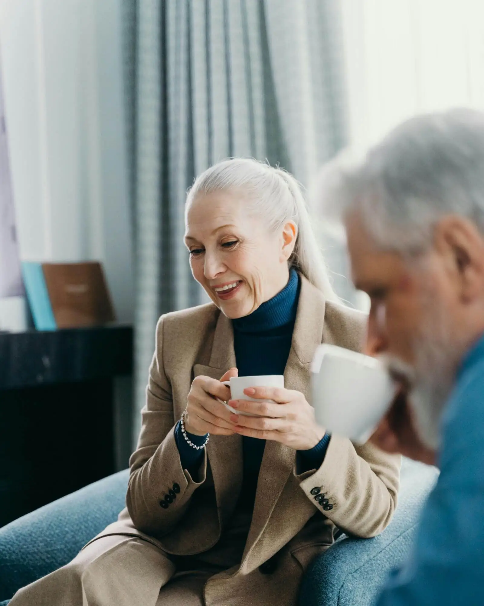 An elderly couple drinking tea in the living room.