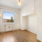 An emptied room in an older home, with built-in cupboards, a wooden floor and a window looking out to trees