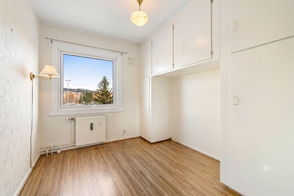 An emptied room in an older home, with built-in cupboards, a wooden floor and a window looking out to trees